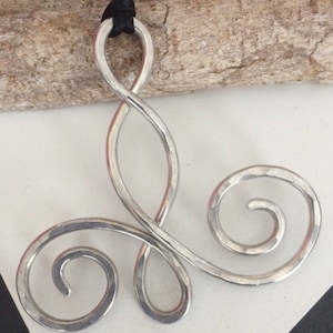 May include: A silver pendant necklace with a triple infinity symbol design. The pendant is made of hammered metal and has a smooth, polished finish.