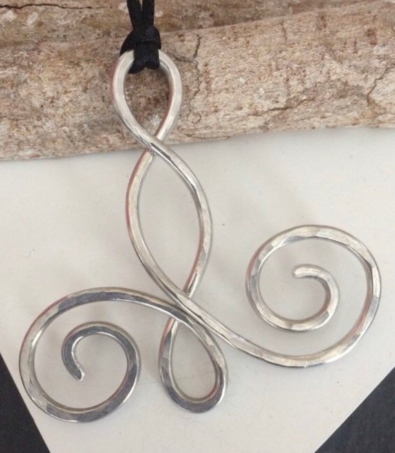 May include: A silver pendant necklace with a triple infinity symbol design. The pendant is made of hammered metal and has a smooth, polished finish.