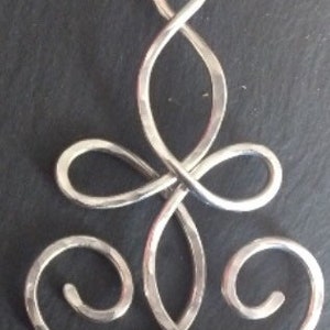 May include: A silver pendant with a Celtic knot design. The pendant is made of hammered metal and has a smooth, polished finish.
