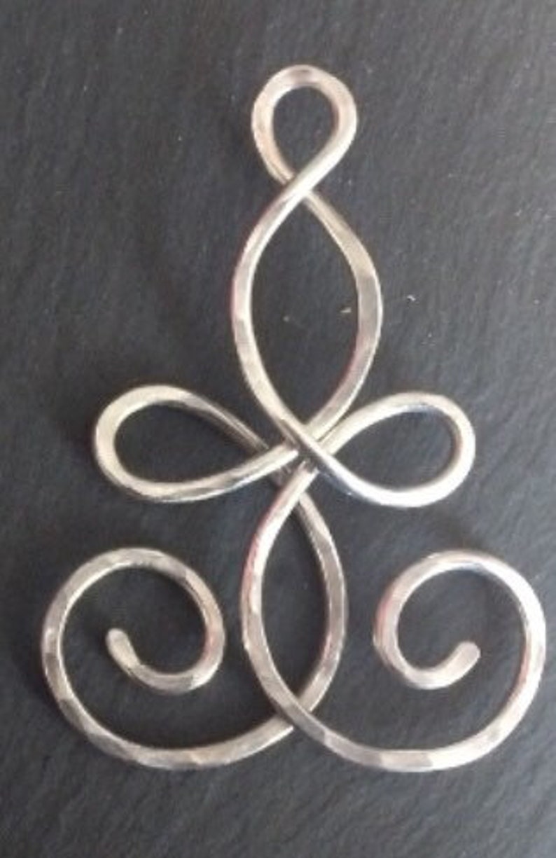 May include: A silver pendant with a Celtic knot design. The pendant is made of hammered metal and has a smooth, polished finish.
