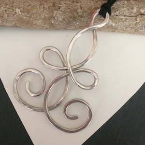 May include: A silver pendant necklace with a swirling, abstract design. The pendant is made of hammered metal and has a textured finish.
