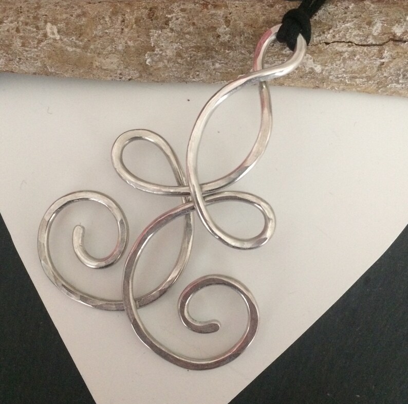 May include: A silver pendant necklace with a swirling, abstract design. The pendant is made of hammered metal and has a textured finish.