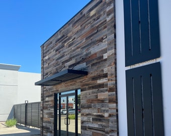 May include: Exterior of a storefront with a wood-paneled wall, black awning, and glass double doors. The storefront has a black metal sign with the text "Man's Garage Est. 2018 Woodworking".