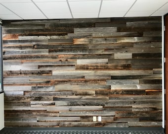 May include: A wall covered in reclaimed wood planks, featuring a variety of wood tones and textures, including gray, brown, and white. The planks are arranged in a horizontal pattern, creating a rustic and industrial look.
