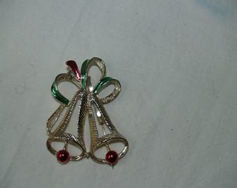 May include: A gold-tone Christmas pin with two bells and a green and red bow. The bells have red accents.