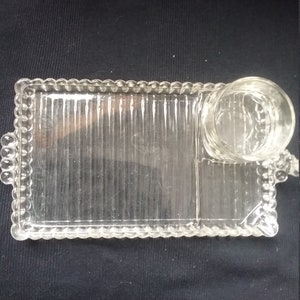 May include: A clear glass serving tray with a beaded edge and a separate glass cup. The tray has a ribbed design and is divided into sections.