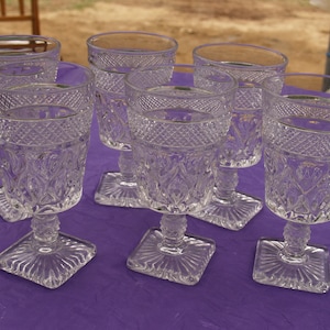 May include: Six clear glass goblets with a cut glass design. The goblets have a square base and a round bowl.