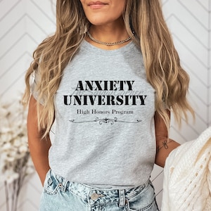 Op de afbeelding: Grijs T-shirt met zwarte tekst die "Anxiety University High Honors Program" luidt.