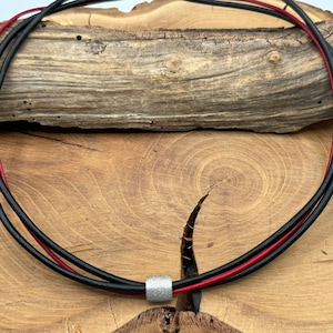 Könnte beinhalten: Eine schwarze und rote Lederkette mit einem silbernen Perlenakzent.