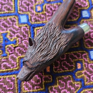 May include: A wooden slingshot with a carved wolf head design. The slingshot is made of dark wood with a natural finish. The wolf's head is detailed with fur and a sharp snout.