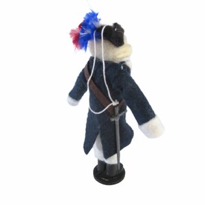 May include: A handmade doll dressed in a dark blue coat with white cuffs and a brown strap. The doll has a white face, black hat, and a decorative feather plume with red and blue accents. A small sword hangs at the doll's side.