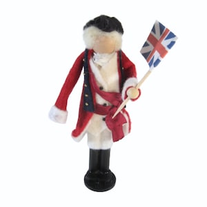 May include: A felt doll dressed in a red coat with gold buttons, a white shirt, and a red sash. The doll is holding a small Union Jack flag.