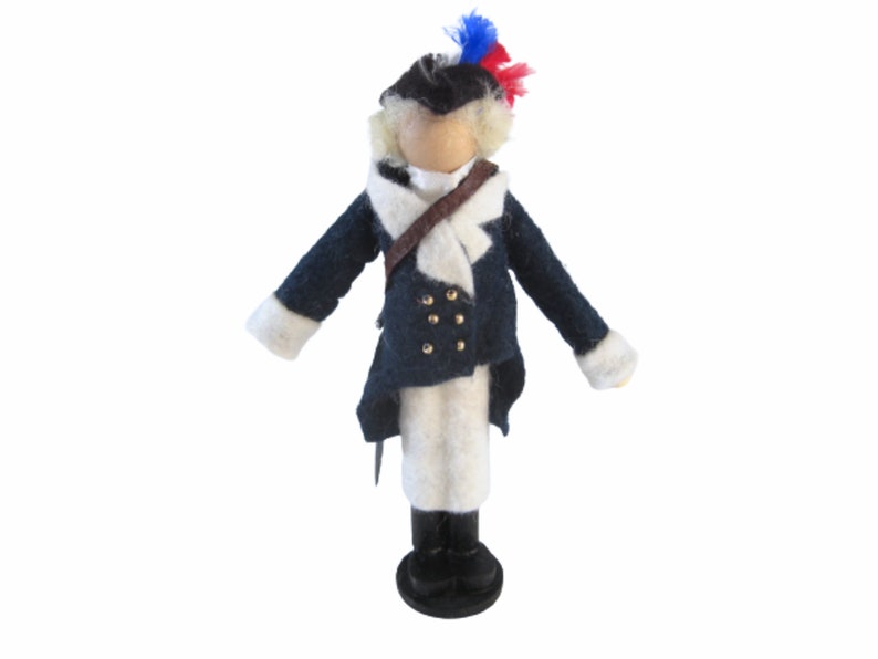 May include: A handcrafted doll dressed in a colonial-era military uniform. The doll features a dark blue coat with gold buttons, white pants, and a tricorn hat with red and blue accents. The doll stands on a black base.