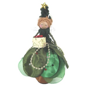 May include: A green Christmas tree fairy doll with brown yarn hair, a green dress, and a gold star on top of her head. She is holding a small gift box.