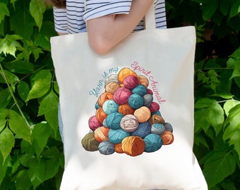 May include: A white tote bag with a colorful illustration of yarn balls stacked in a pyramid shape. The text "Yarn is my Spirit Animal" is written around the yarn balls.