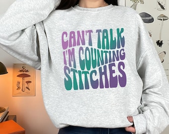 May include: A gray sweatshirt with a colorful graphic that says "Can't Talk I'm Counting Stitches".