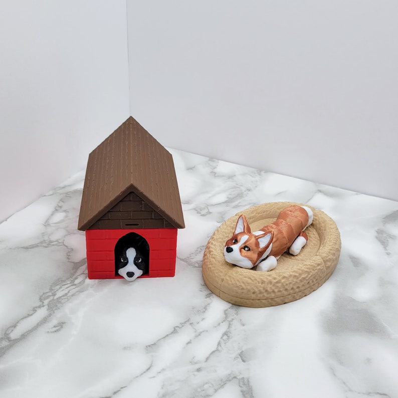 May include: A brown and red dog house with a black and white dog peeking out of the door. A brown and white dog is lying in a brown bed.