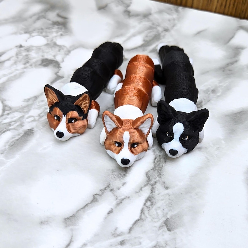 May include: Three 3D printed corgi dog figurines. One is black and white, one is brown and white, and one is copper and white.
