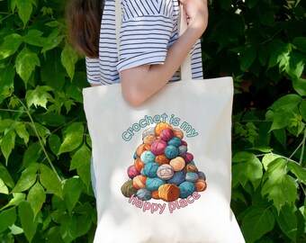 May include: A white tote bag featuring a colourful illustration of balls of yarn and the text "Crochet is my happy place".