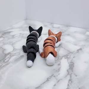 May include: Two small, curled-up, black and brown dog figurines with white accents. The black dog is on the left and the brown dog is on the right. Both dogs are facing the same direction.