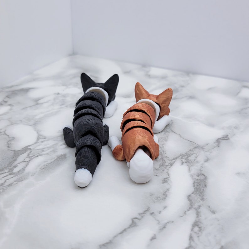 May include: Two small, curled-up, black and brown dog figurines with white accents. The black dog is on the left and the brown dog is on the right. Both dogs are facing the same direction.