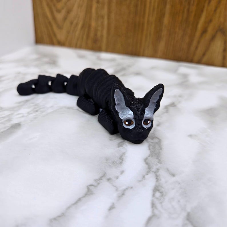 Op de afbeelding: Een zwart-wit 3D-geprint kattenbeeldje met een gesegmenteerd lichaam. De kat heeft een zwart lichaam met witte markeringen rond de ogen en oren.
