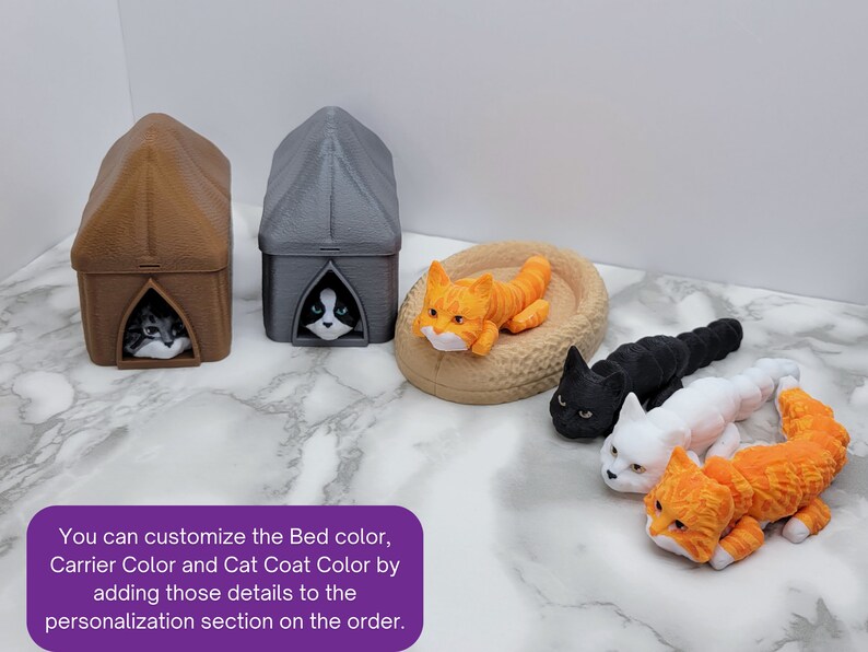 Op de afbeelding: Een set van drie kattenmanden, een bruin, een grijs en een beige. De manden zijn gevormd als kleine huisjes met een kat die uit de ingang kijkt. Er liggen ook vier katten, een oranje, een zwarte, een witte en een oranje-witte. De tekst op de afbeelding luidt: "U kunt de kleur van het bed, de kleur van de drager en de kleur van de vacht van de kat aanpassen door deze details toe te voegen aan het personalisatiesectie van de bestelling."