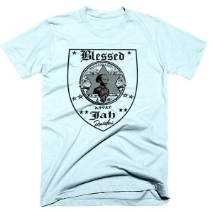 Puede incluir: Camiseta azul claro con un gráfico en blanco y negro de un escudo con una estrella y las palabras "Blessed", "Jah Rastafari" y la cara de un niño dentro.