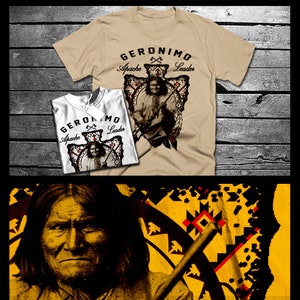 Può includere: Una maglietta color beige con una stampa grafica di un uomo nativo americano che tiene un fucile. La grafica è circondata da un motivo geometrico rosso, bianco e nero. Il testo "Geronimo Apache Leader" è stampato sulla maglietta.