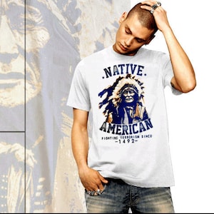 May include: White t-shirt with a blue and white graphic of a Native American man wearing a headdress. The text "NATIVE AMERICAN FIGHTING TERRORISM SINCE -1492- " is printed on the shirt.