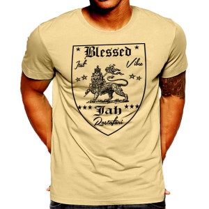 Puede incluir: Una camiseta beige con un gráfico negro de un león con una corona y las palabras "Blessed Vibes Jah Rastafari" en forma de escudo.