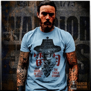 Puede incluir: Una camiseta azul claro con una calavera que lleva un sombrero cónico y el texto "Big Trouble in Little China" y "The Three Storms".