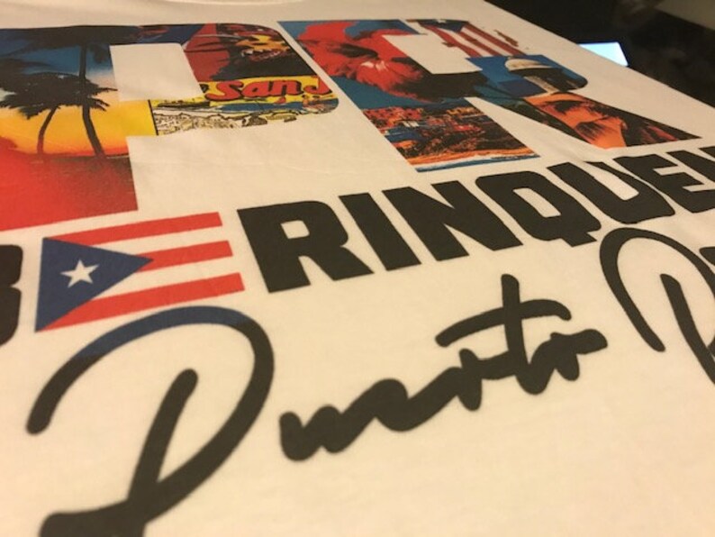 May include: White t-shirt with a black and white graphic design featuring the text "Puerto Rico" and a red, white, and blue Puerto Rican flag. The graphic design also includes a collage of images of Puerto Rico.