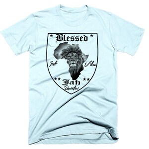 Puede incluir: Camiseta azul claro con un gráfico negro de una cabeza de león dentro de un contorno del continente africano. El gráfico también incluye el texto "Blessed", "Jah Rastafari", "Iat" y "Vibe".