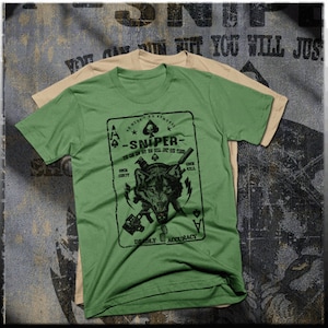 May include: Green t-shirt featuring a playing card graphic with a wolf, guns, and knives. The card reads "No Mercy, No Remorse - Sniper - You Can Run But You Will Just Die Tired. One Shot, One Kill. Deadly Accuracy."