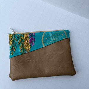 May include: A small brown zippered pouch with a teal fabric lining featuring a dreamcatcher and feather pattern.