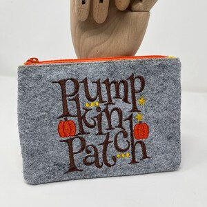 May include: Gray felt zippered pouch with the embroidered text "Pumpkin Patch" in brown with orange pumpkins and yellow stars.