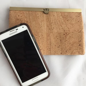 May include: A brown cork wallet with a gold metal clasp and a white Samsung smartphone.