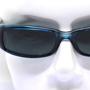 May include: Blue rectangular sunglasses with dark lenses. The frames have a glossy finish and a slight wrap-around design. The sunglasses are displayed on a white mannequin head.