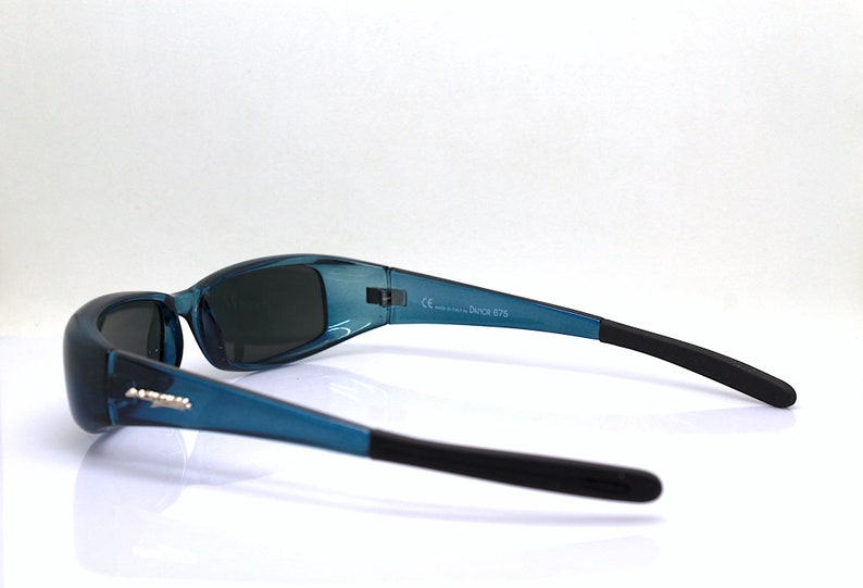 May include: Teal-colored sunglasses with black temples. The sunglasses have a curved design and dark lenses. The text "DUTCH 675" is printed on the frame. The sunglasses are shown against a white background.