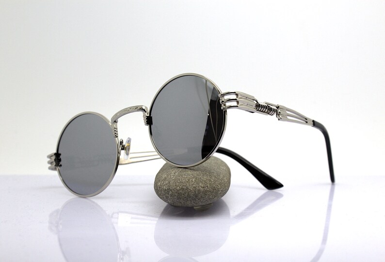K&ouml;nnte beinhalten: Silberne runde Sonnenbrille mit einem einzigartigen, filigranen und detaillierten Metallrahmen. Die Sonnenbrille hat dunkelgraue Gl&auml;ser.