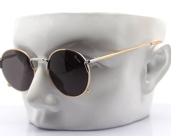 May include: Round sunglasses with gold rims and dark lenses. The sunglasses are displayed on a white mannequin head.