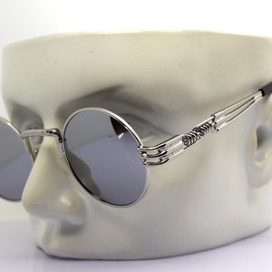K&ouml;nnte beinhalten: Silberne runde Sonnenbrille mit einem einzigartigen, filigranen und detaillierten Metallrahmen. Die Sonnenbrille hat verspiegelte Gl&auml;ser.