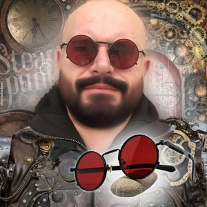 K&ouml;nnte beinhalten: Schwarze runde Sonnenbrille mit roten Gl&auml;sern im Steampunk-Stil. Die Brille hat einen d&uuml;nnen Metallrahmen. Der Hintergrund zeigt Zahnr&auml;der und eine Uhr, mit dem Wort "Steampunk" sichtbar.