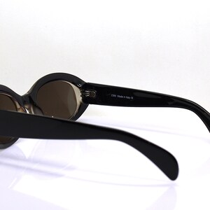 May include: Black oval sunglasses with brown lenses. The sunglasses have a black plastic frame and are made in Italy.