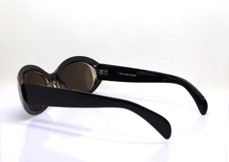 May include: Black oval sunglasses with brown lenses. The sunglasses have a black plastic frame and are made in Italy.