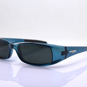 May include: Blue sunglasses with dark lenses. The frames have a translucent blue finish with black accents on the temples and bridge. The sunglasses are designed for eye protection and fashion.
