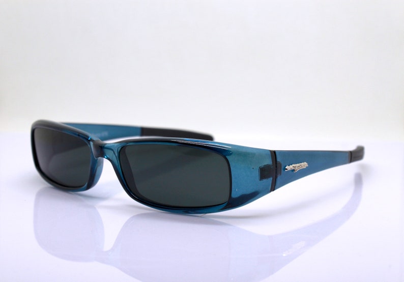 May include: Blue sunglasses with dark lenses. The frames have a translucent blue finish with black accents on the temples and bridge. The sunglasses are designed for eye protection and fashion.