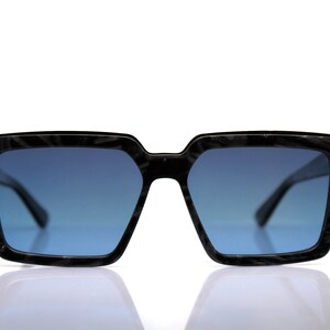 May include: Black sunglasses with a dark blue lens and a textured frame.