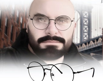 May include: A pair of black round spectacles with a thin metal frame. The glasses are sitting on a white surface.